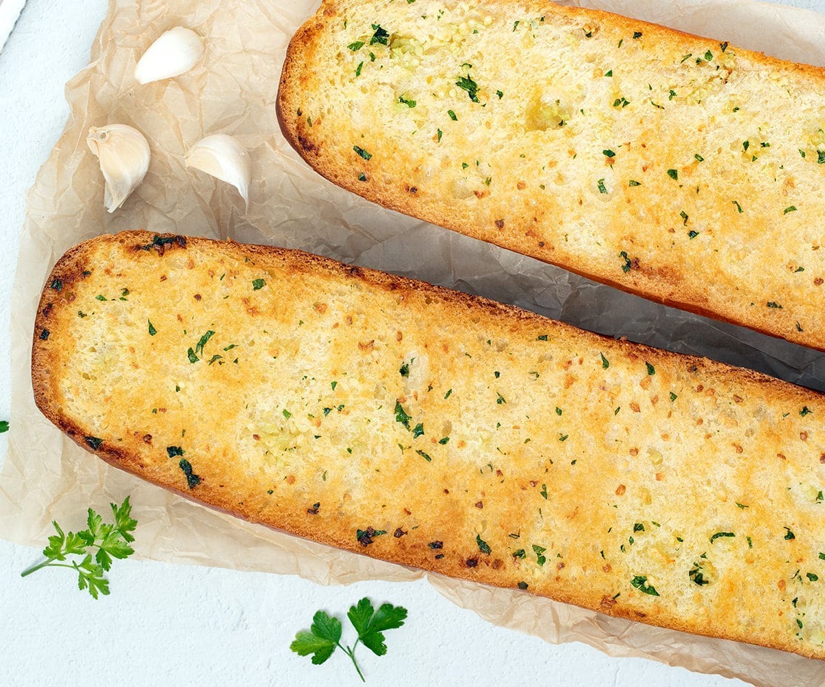 Homemade Garlic Bread Recipe 7 Homemade Garlic Bread recipe next to garlic cloves and parsley.