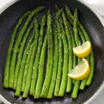 Sautéed Asparagus and lemon wedges in a black skillet.