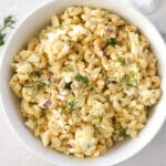 Deviled egg pasta salad in a white bowl next to fresh dill.