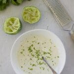 Small bowl of cilantro lime crema with a grater and juiced lime.