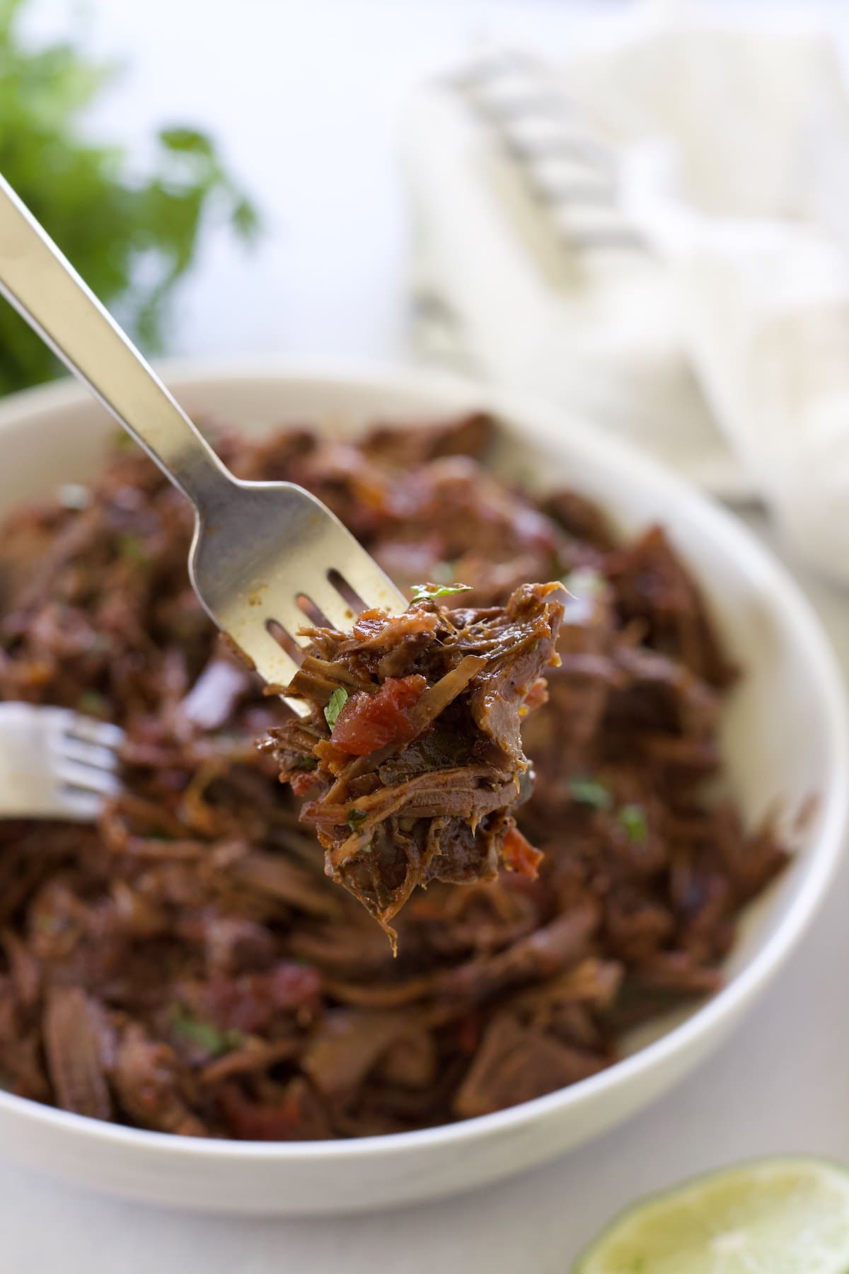 Two forks shredding chuck roast in a white bowl.