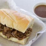 French dip sandwich next to a cup of au jus.
