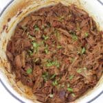 Cream dutch oven full of Mexican shredded beef.