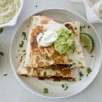 Shredded beef quesadillas on a white plate topped with sour cream and guacamole.