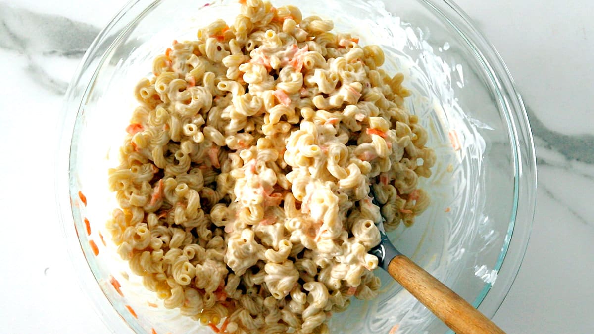 Wooden spoon stirring macaroni salad.