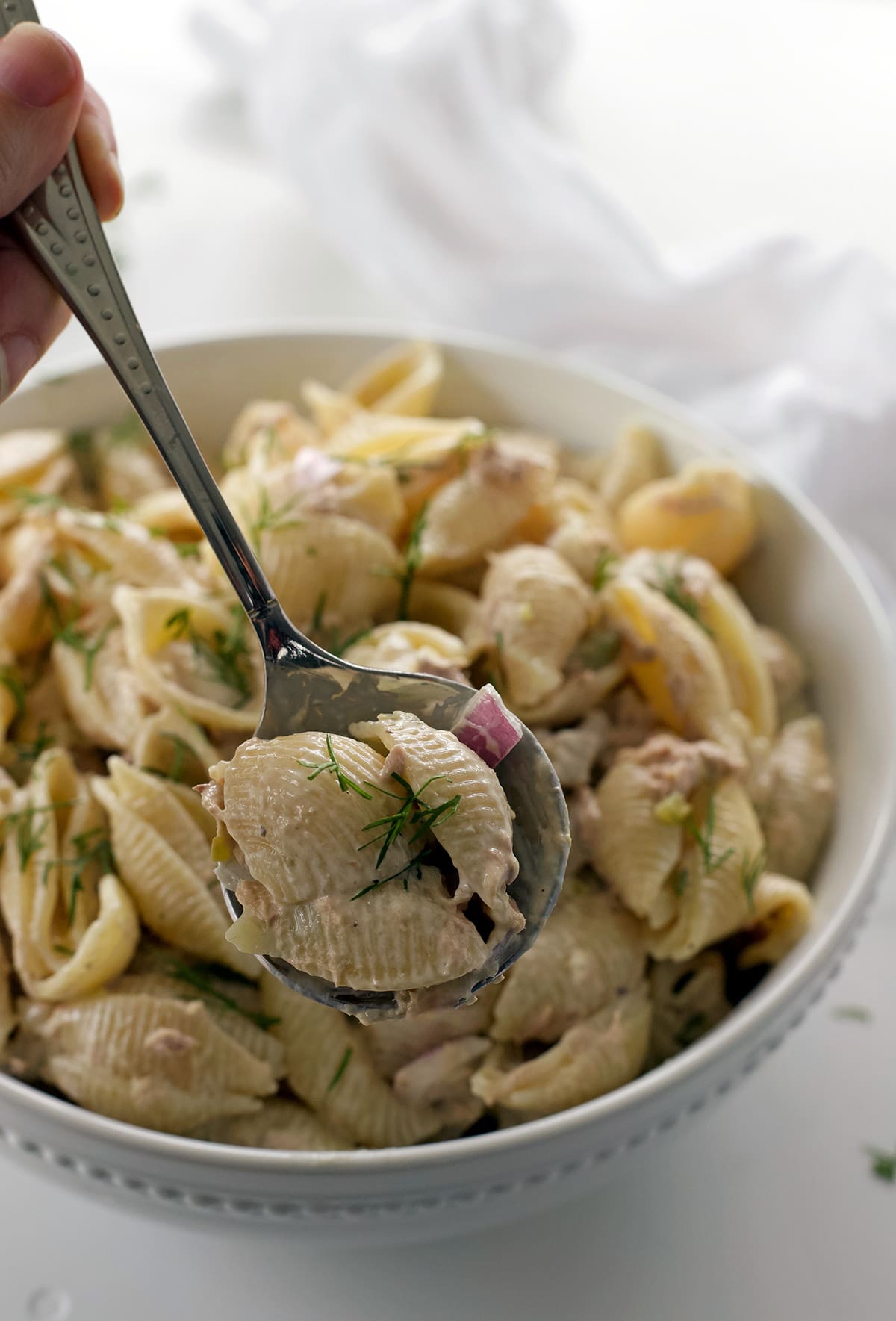 Hand holding a spoon full of cold tuna pasta salad.