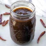 Mason jar full of homemade enchilada sauce surrounded by dried chiles.