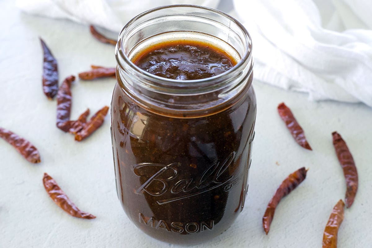 Mason jar full of homemade enchilada sauce surrounded by dried chiles.