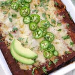 Tray of shredded beef enchiladas topped with jalapenos and avocado slices.