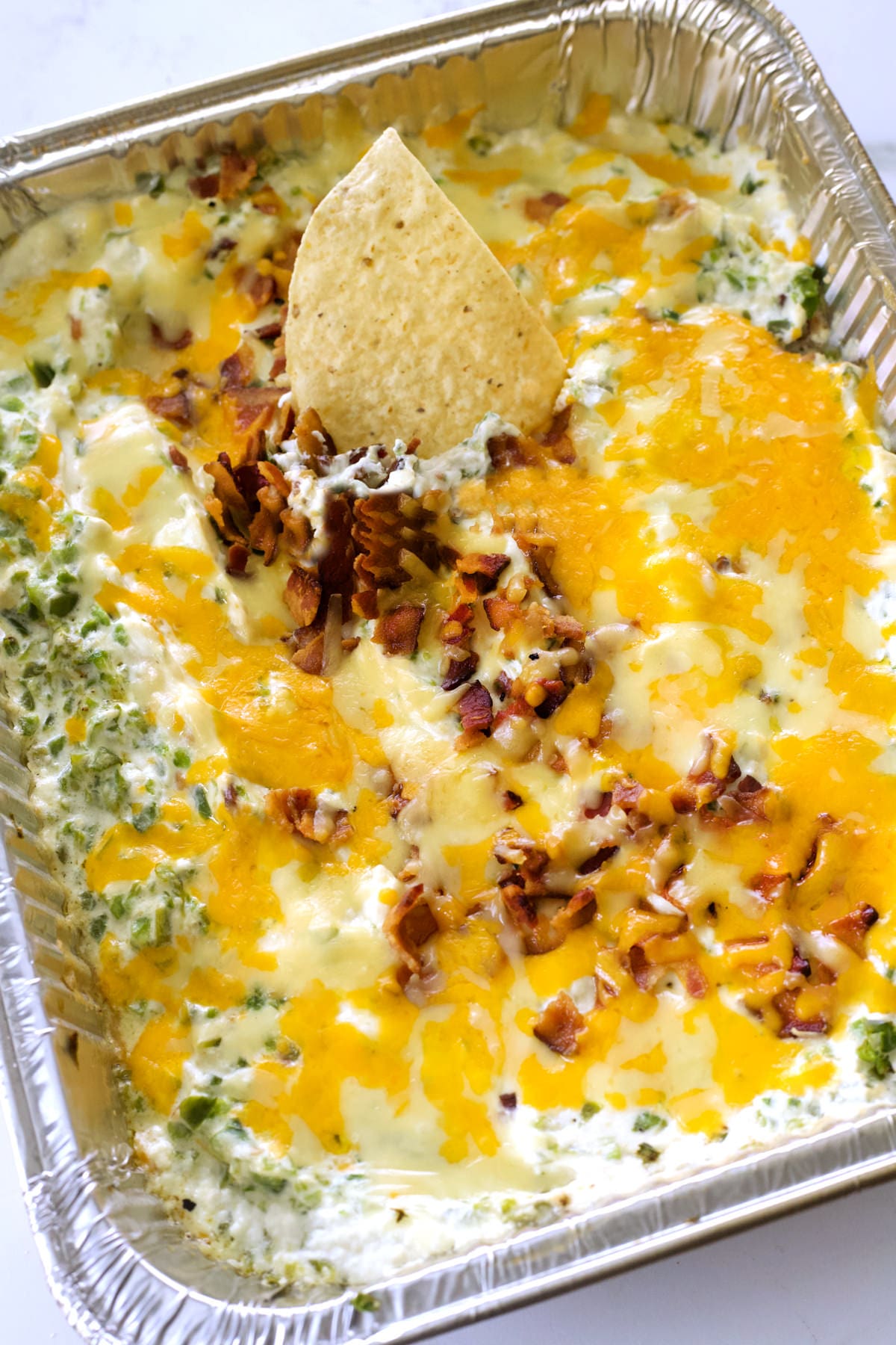 Cooked cream cheese dip with a tortilla chip scooping some up.