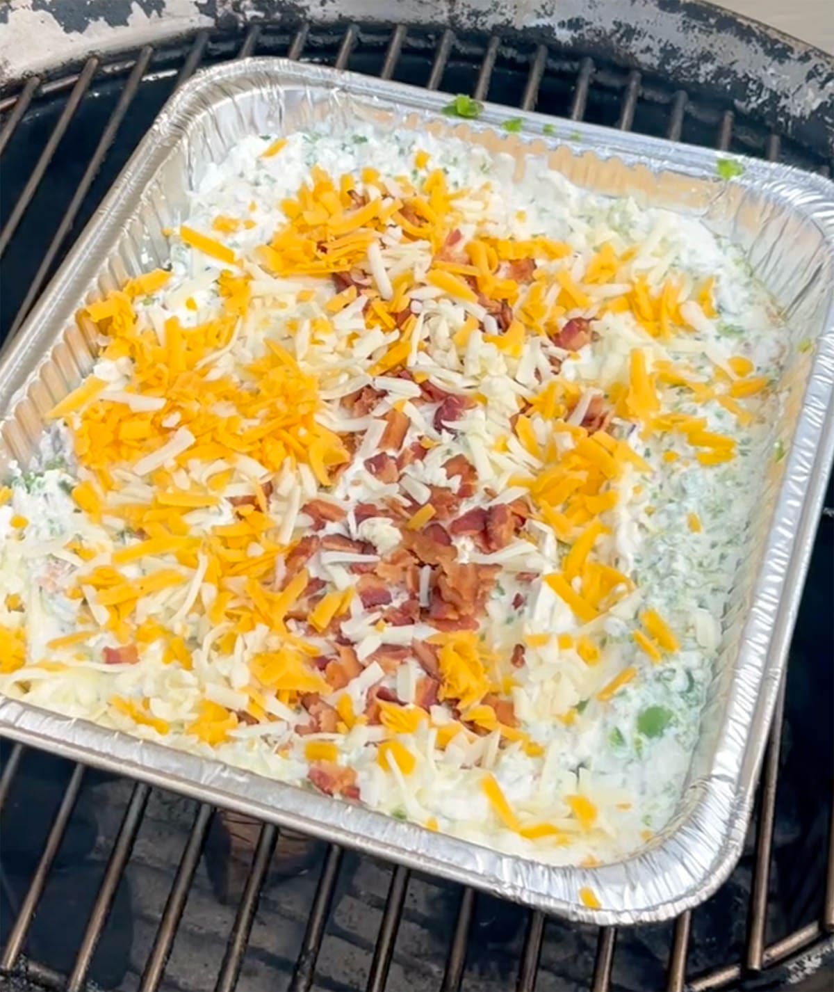 Bacon and cheese on top of a dip on a grill.