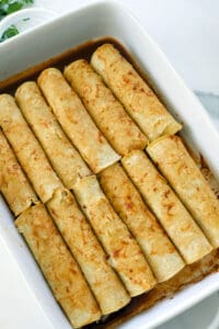Rolled enchiladas in a white baking dish.