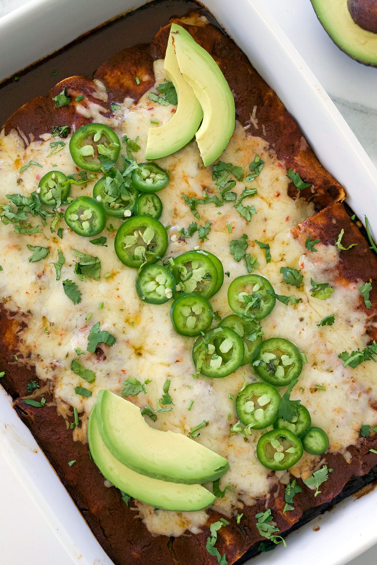 Tray of shredded beef enchiladas topped with jalapenos and avocado slices.