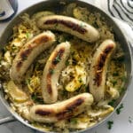 Bratwurst and Sauerkraut in a silver skillet next to German beer.