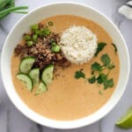 Red curry bowl topped with fresh herbs and vegetables.