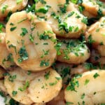 White bowl full of German Potato Salad garnished with parsley.