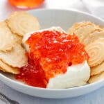 Plate of pepper jelly and cream cheese dip surrounded by crackers.